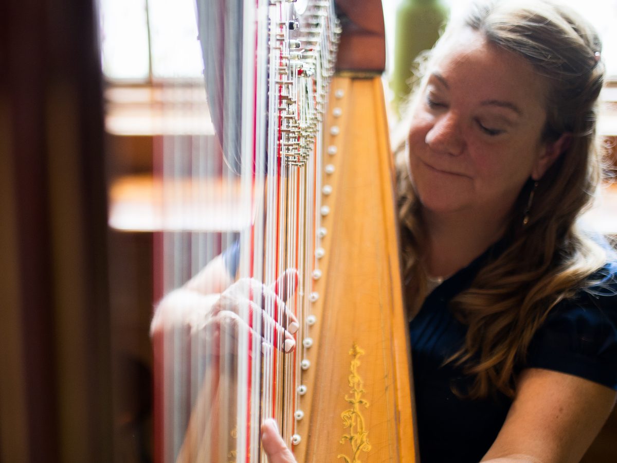 Patricia Turse playing her harp in window light, eyes closed